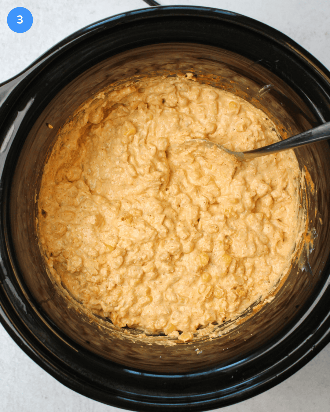 Step 3 of Mexican street corn dip: The dip is shown in the slow cooker after stirring. It is a creamy yellow corn dip.