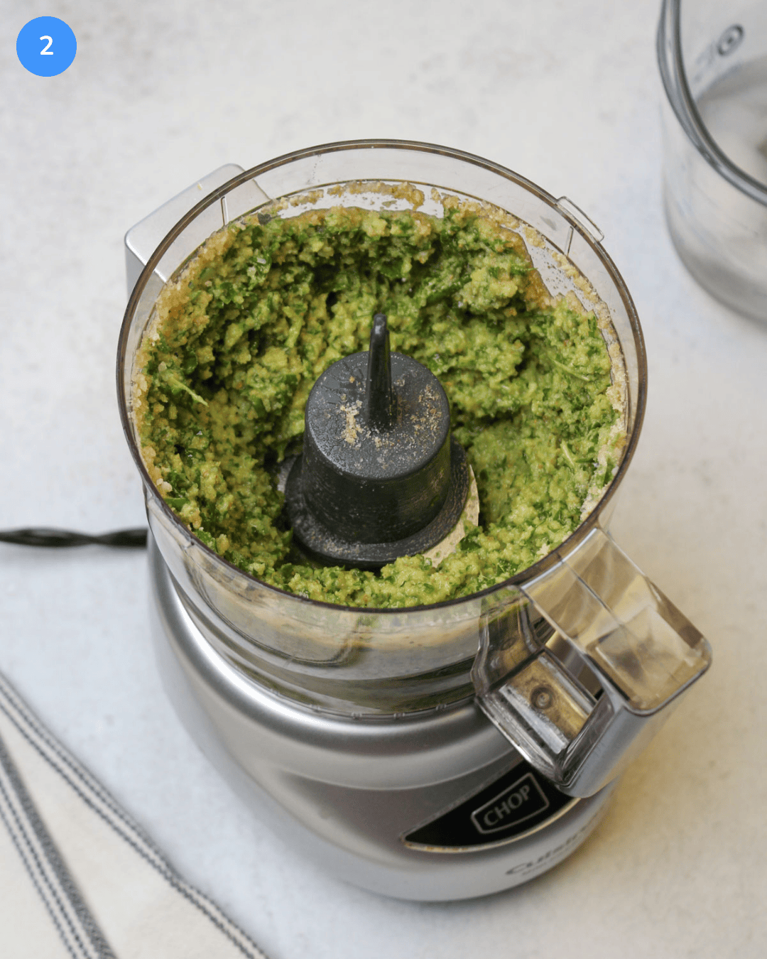 A food processor with partially mixed basil pesto in it.