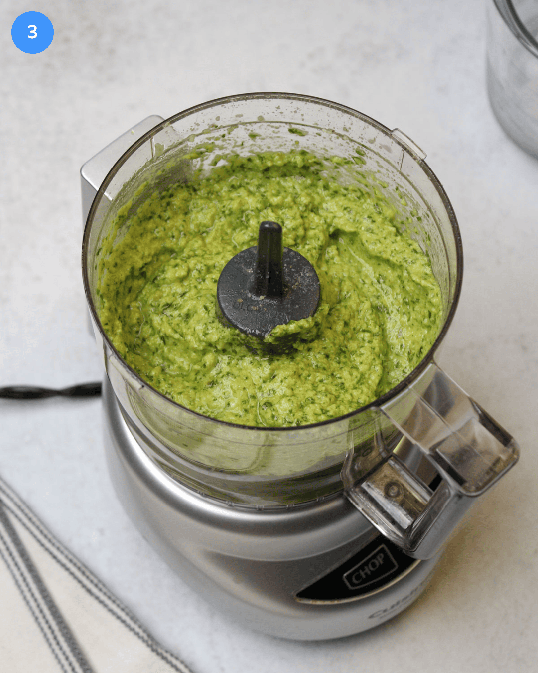 A food processor with freshly made creamy basil pesto in it.