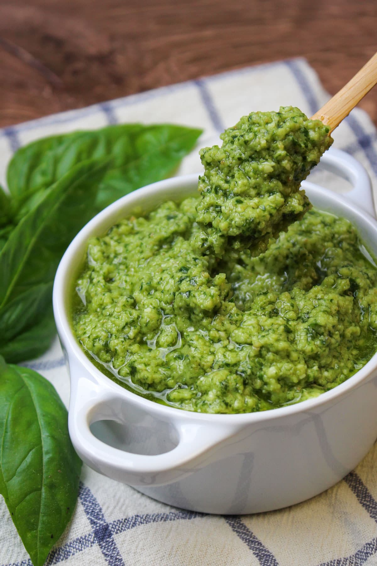 A small spoonful of freshly made nut free basil pesto being scooped out of a white ceramic bowl.