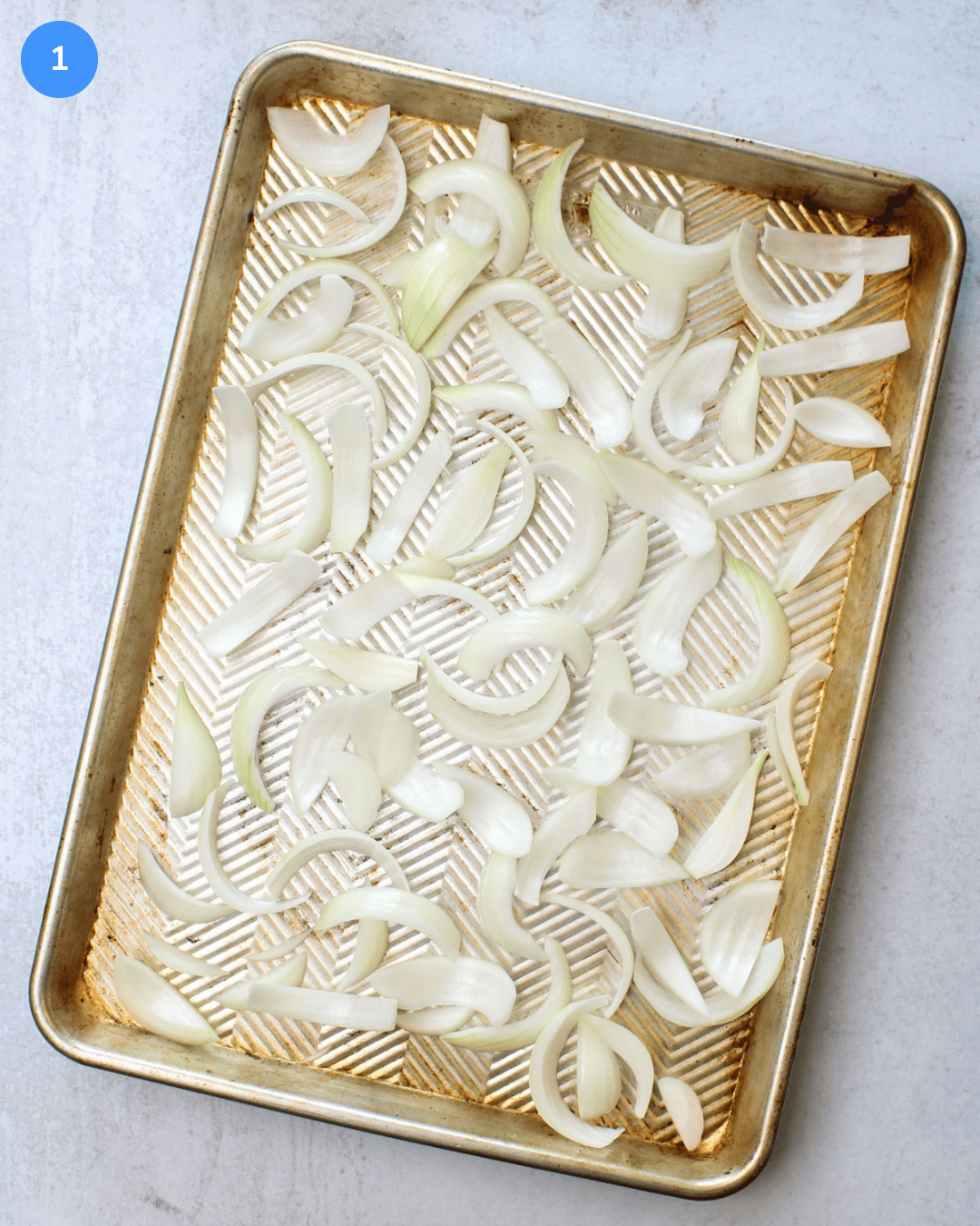 An aluminum sheet pan with sliced vidalia onion on it.