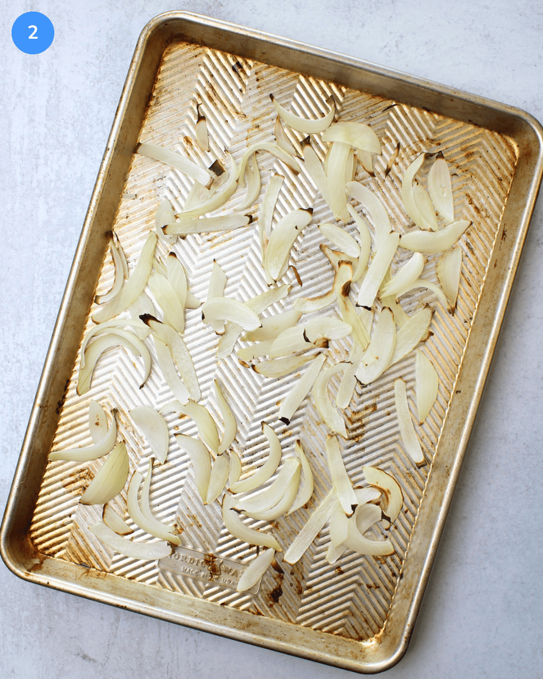 An aluminum sheet pan with charred vidalia onion slices on it.