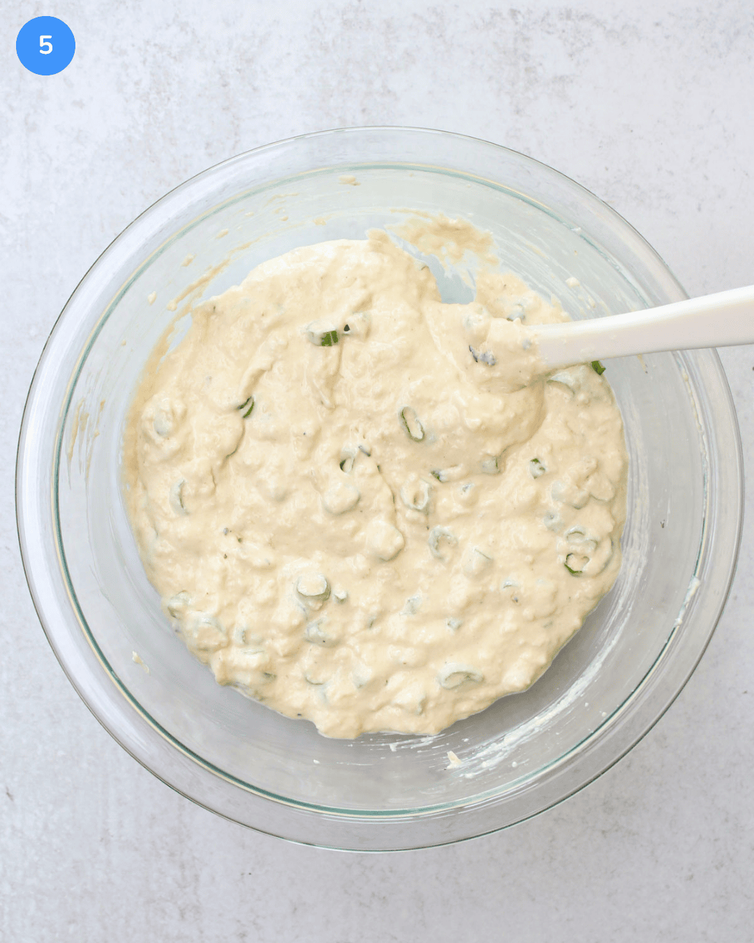 A glass mixing bowl with creamy onion dip and scallions in it.