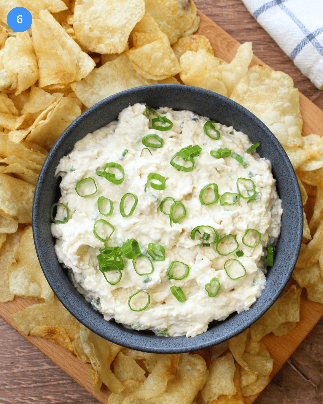 A blue stone bowl of creamy vidalia onion dip served on a wooden board with kettle chips.