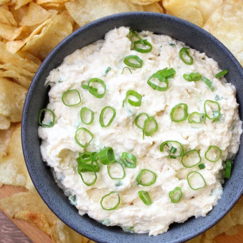 A blue stone bowl of creamy onion dip garnished with scallions, served with kettle chips.