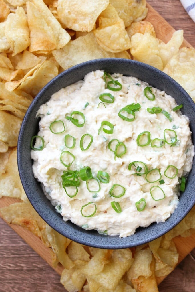 A blue stone bowl of creamy onion dip garnished with scallions, served with kettle chips.