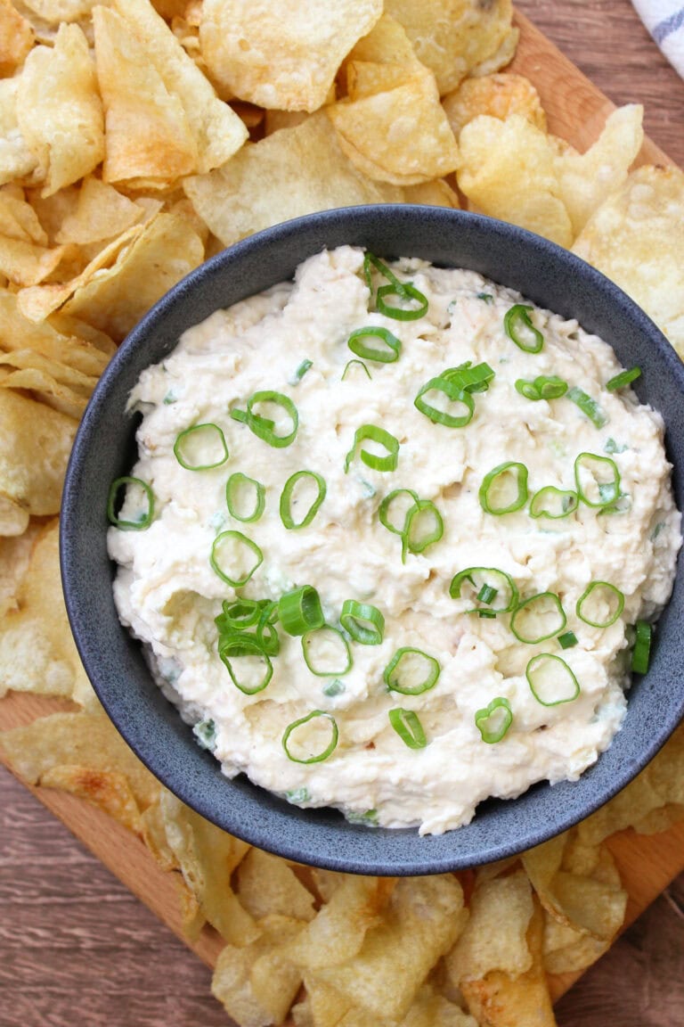 A blue stone bowl of creamy onion dip garnished with scallions, served with kettle chips.