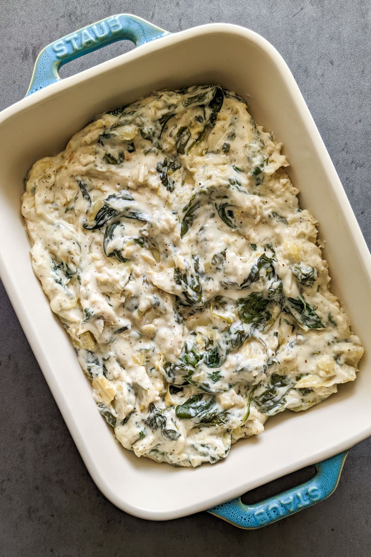 A ceramic baking dish of creamy spinach and artichoke dip.