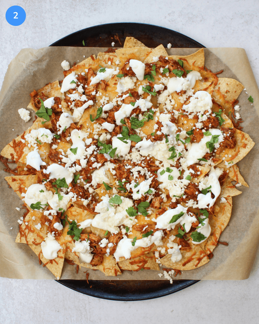 How to make chicken tinga nachos step 2: The nachos after being baked and topped with greek yogurt crema, queso fresco, and fresh cilantro.