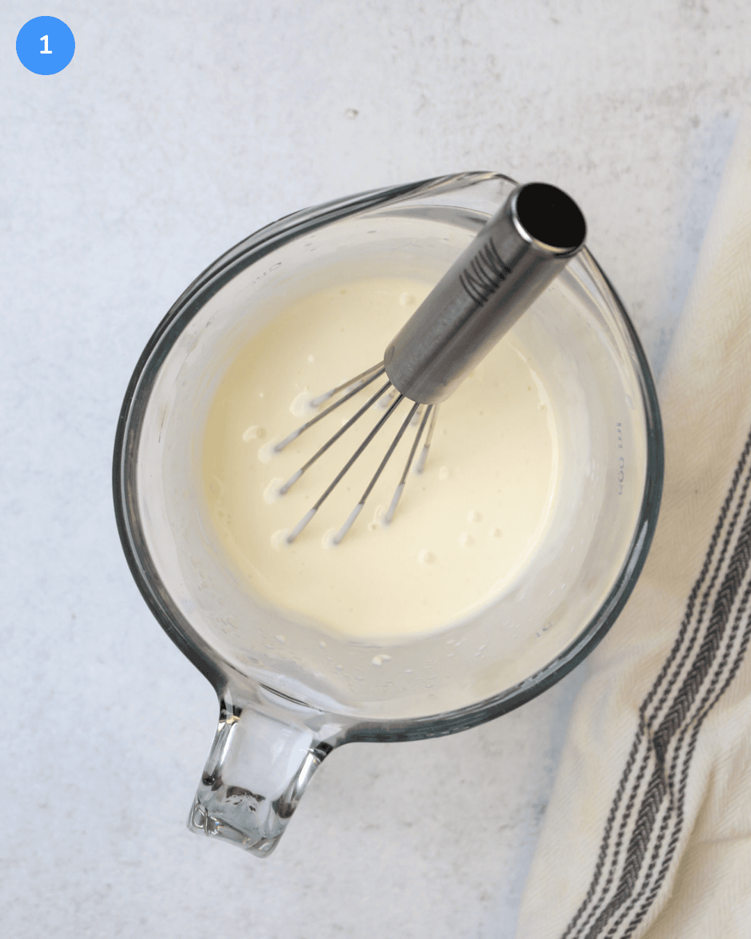 A glass liquid measuring cup with a mixture of mayo, lime juice, and water being whisked in it.