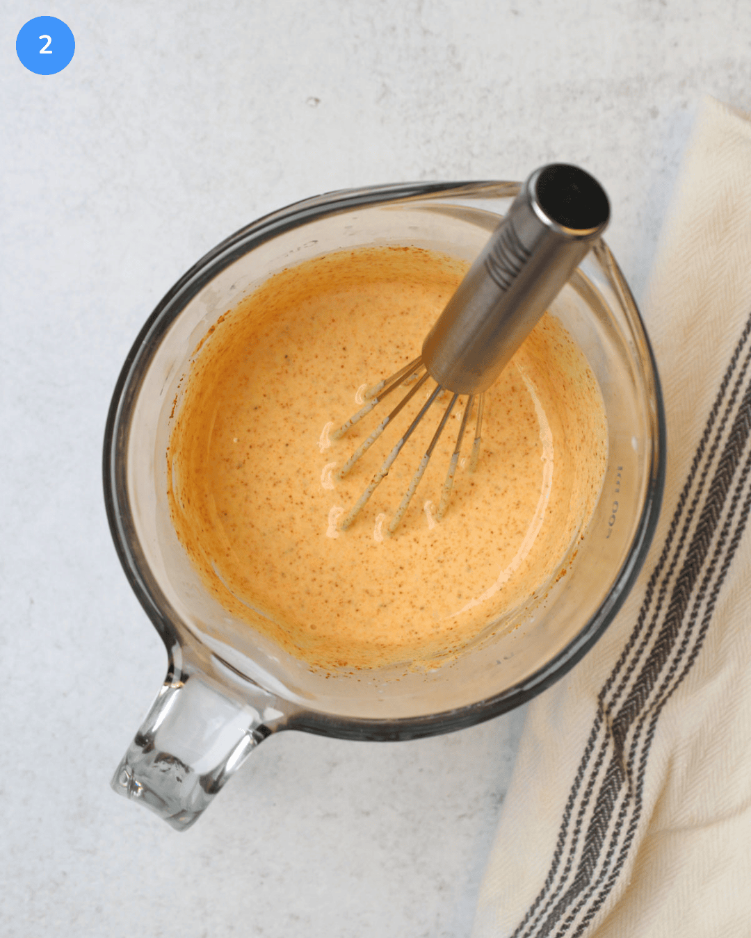 A glass liquid measuring cup with freshly whisked chili lime dressing in it.