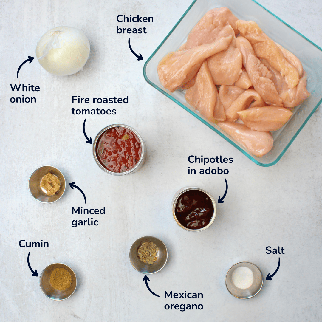 The ingredients for crockpot chicken tinga showling white onion, chicken breast, fire roasted tomatoes, minced garlic, chipotles in adobo, salt, mexican oregano, and cumin.