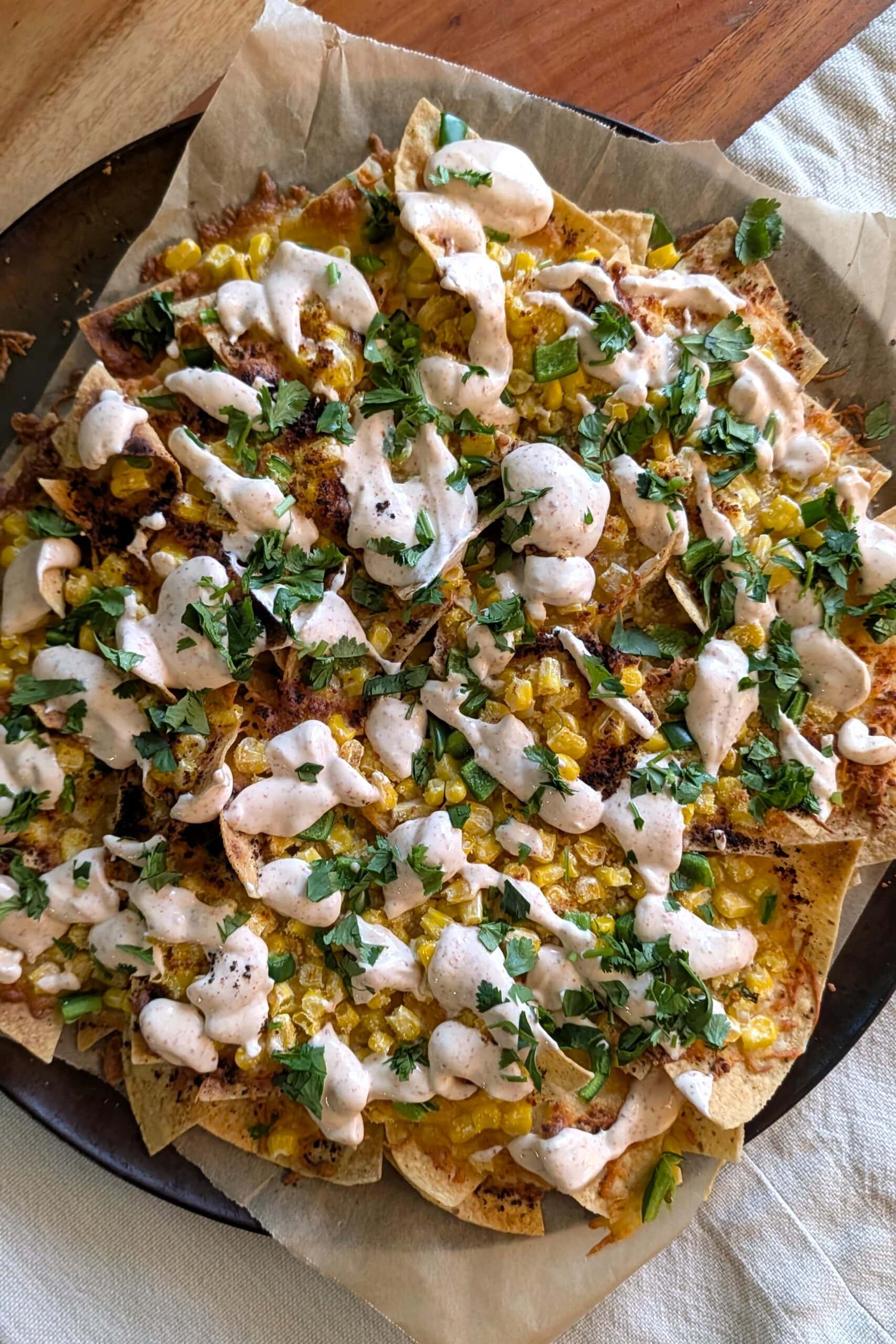 A round tray of freshly baked elote nachos drizzled with Tajin lime aioli.