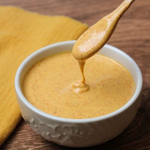 A white ceramic bowl with freshly made chili lime dressing in it, being drizzled off a wooden spoon.