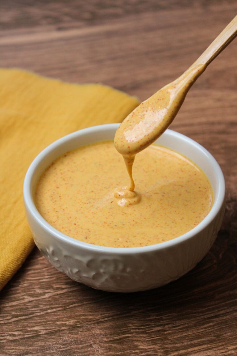 A white ceramic bowl with freshly made chili lime dressing in it, being drizzled off a wooden spoon.