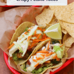 A takeout basket of two potato tacos on corn tortillas, served with tortilla chips and a lime wedge, with a title overlaid.