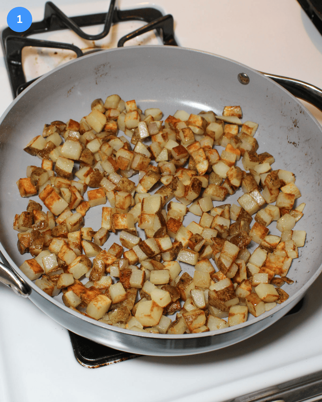 A ceramic saute pan with crispy diced potatoes cooking on the stove.