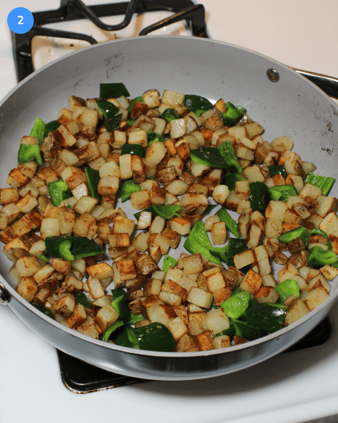 A ceramic saute pan with crispy potatoes and poblanos cooking on the stove.