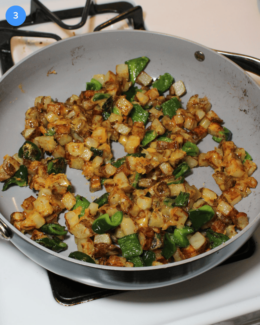 A ceramic saute pan with cheesy potatoes and poblanos cooking on the stove.