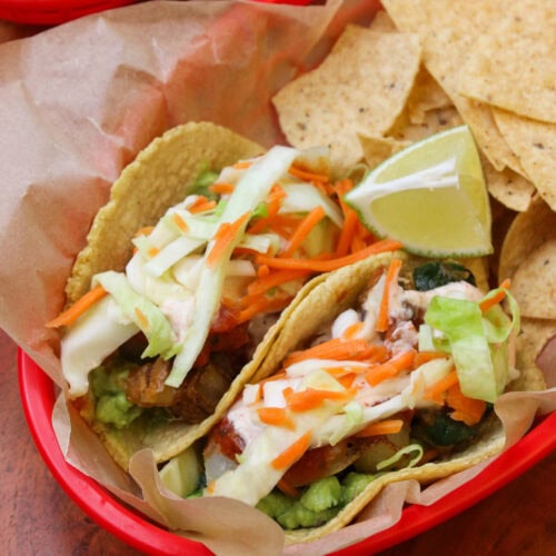 A red takeout basket lined with parchment serving two freshly made potato poblano tacos and tortilla chips.