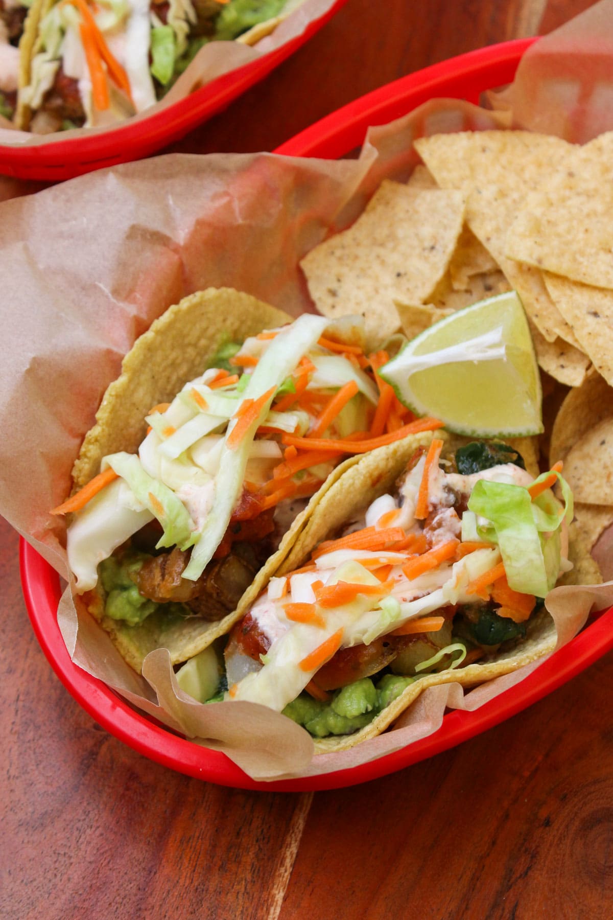 A red takeout basket lined with parchment serving two freshly made potato poblano tacos and tortilla chips.