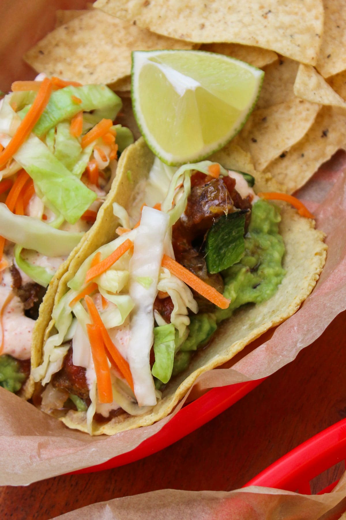 A crispy potato and poblano taco topped with guacamole, crema, salsa, and slaw, served with a lime wedge and tortilla chips.