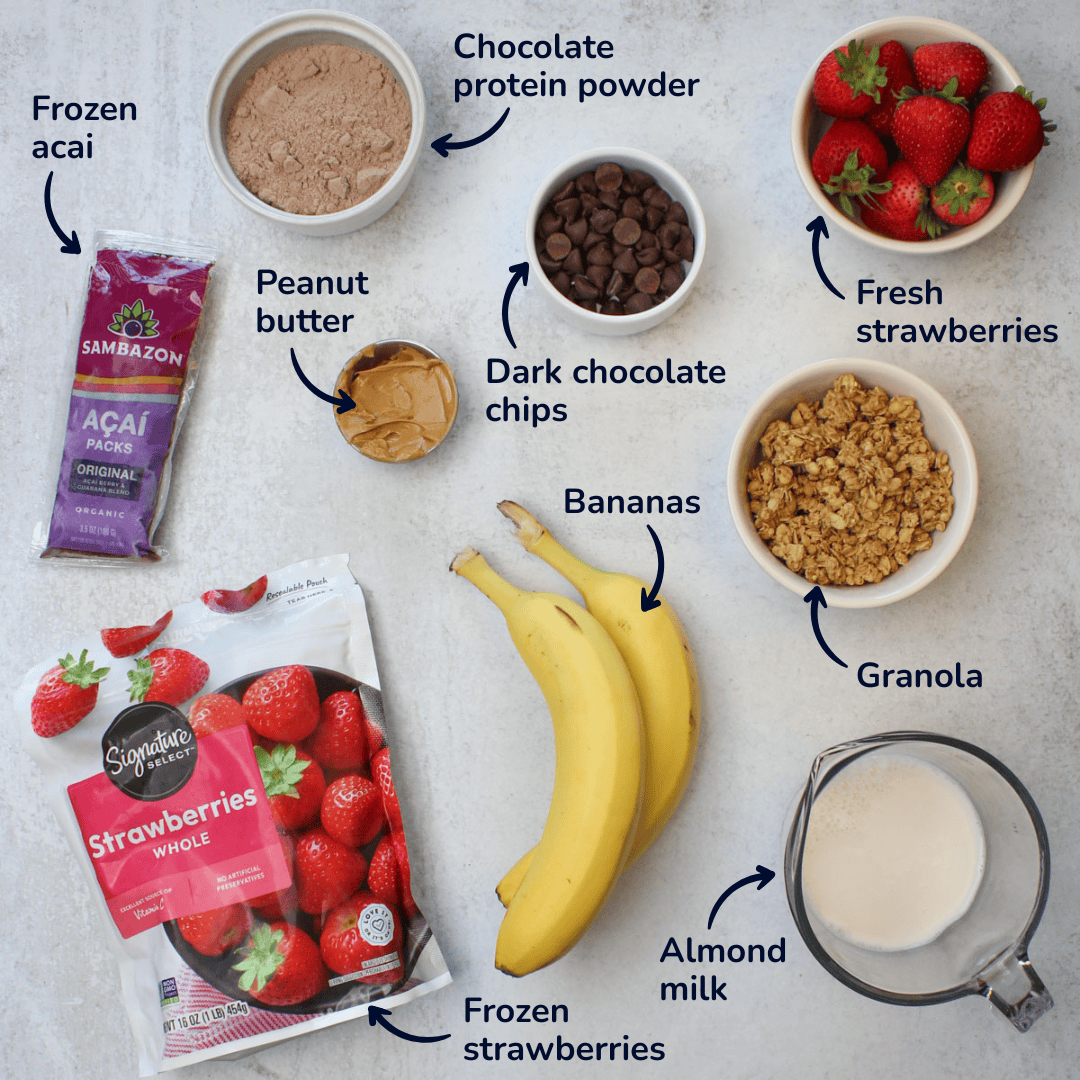 Ingredients for making high protein acai bowls: frozen acai, frozen strawberries, bananas, almond milk, peanut butter, chocolate protein powder, fresh strawberries, granola, and dark chocolate chips.