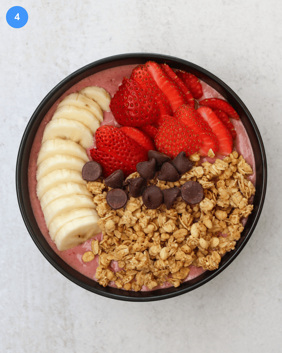 A high protein acai bowl topped with fresh strawberry and banana slices, dark chocolate chips, and granola.