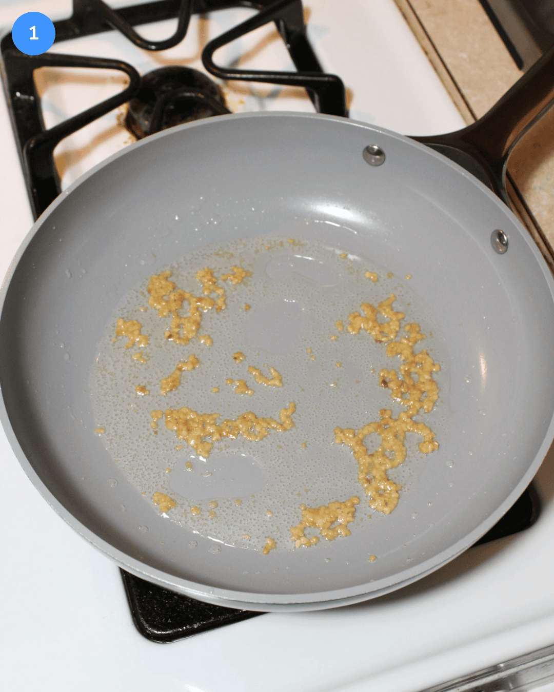 Minced garlic cooking in oil in a nonstick ceramic frying pan on the stove.