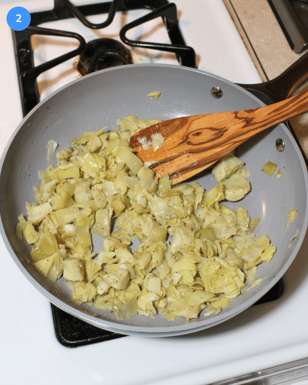 Artichokes cooking in a ceramic frying pan on the stove.