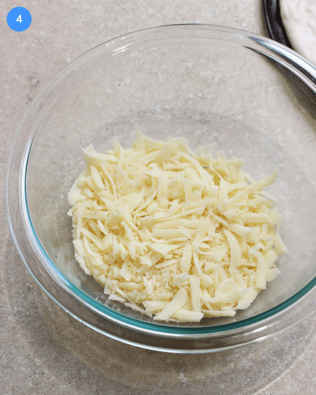 A glass mixing bowl filled with shredded mozzarella and grated parmesan.