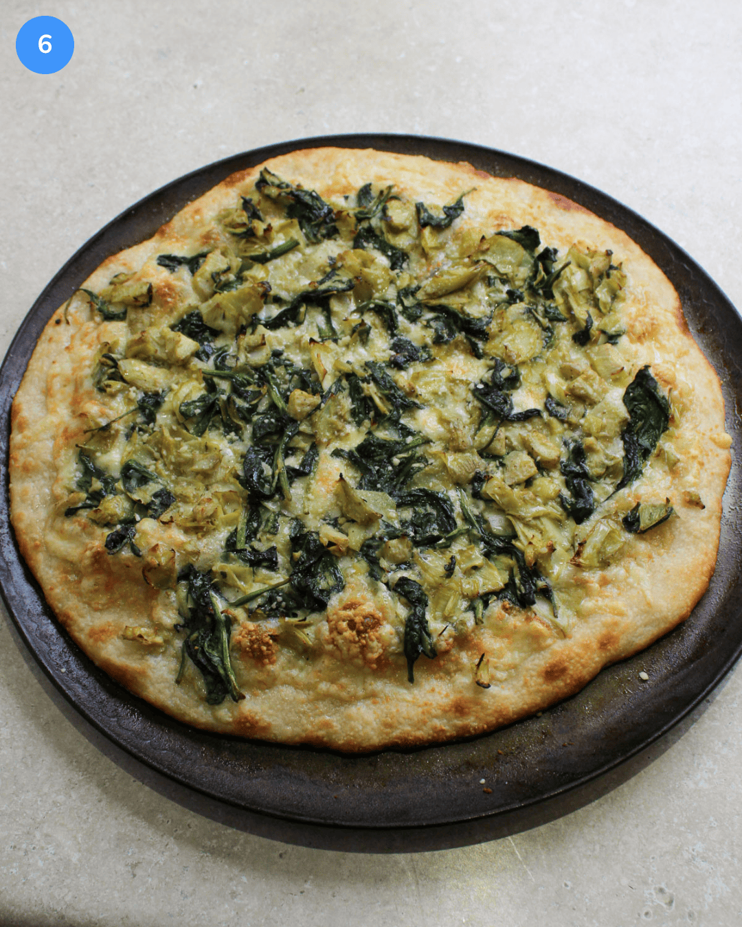 A freshly baked spinach and artichoke pizza on a metal pizza pan.