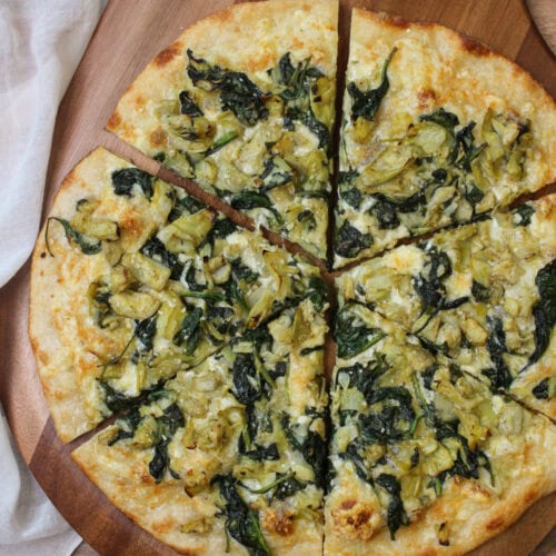 A freshly baked spinach artichoke pizza on a wooden pizza peel.
