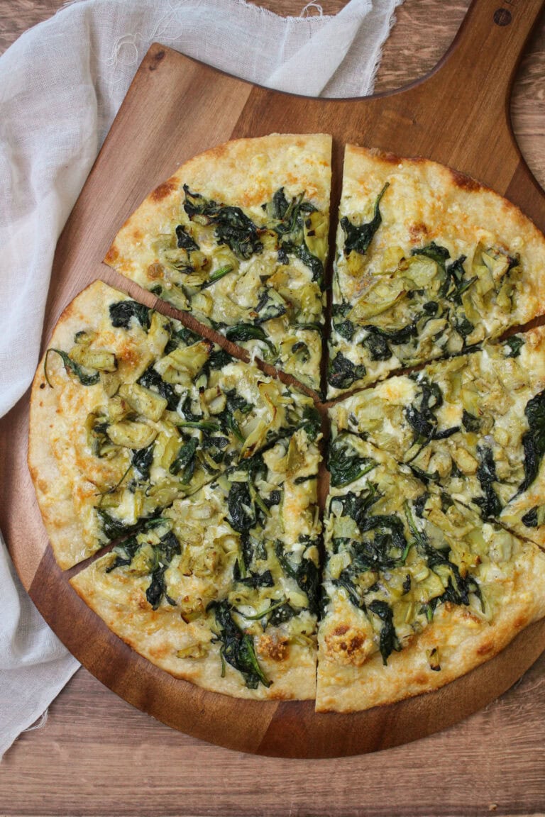 A freshly baked spinach artichoke pizza on a wooden pizza peel.