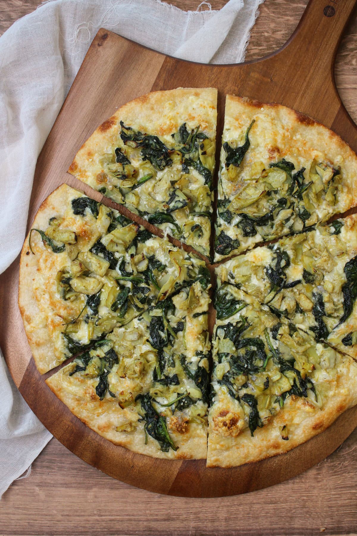 A freshly baked spinach artichoke pizza on a wooden pizza peel.