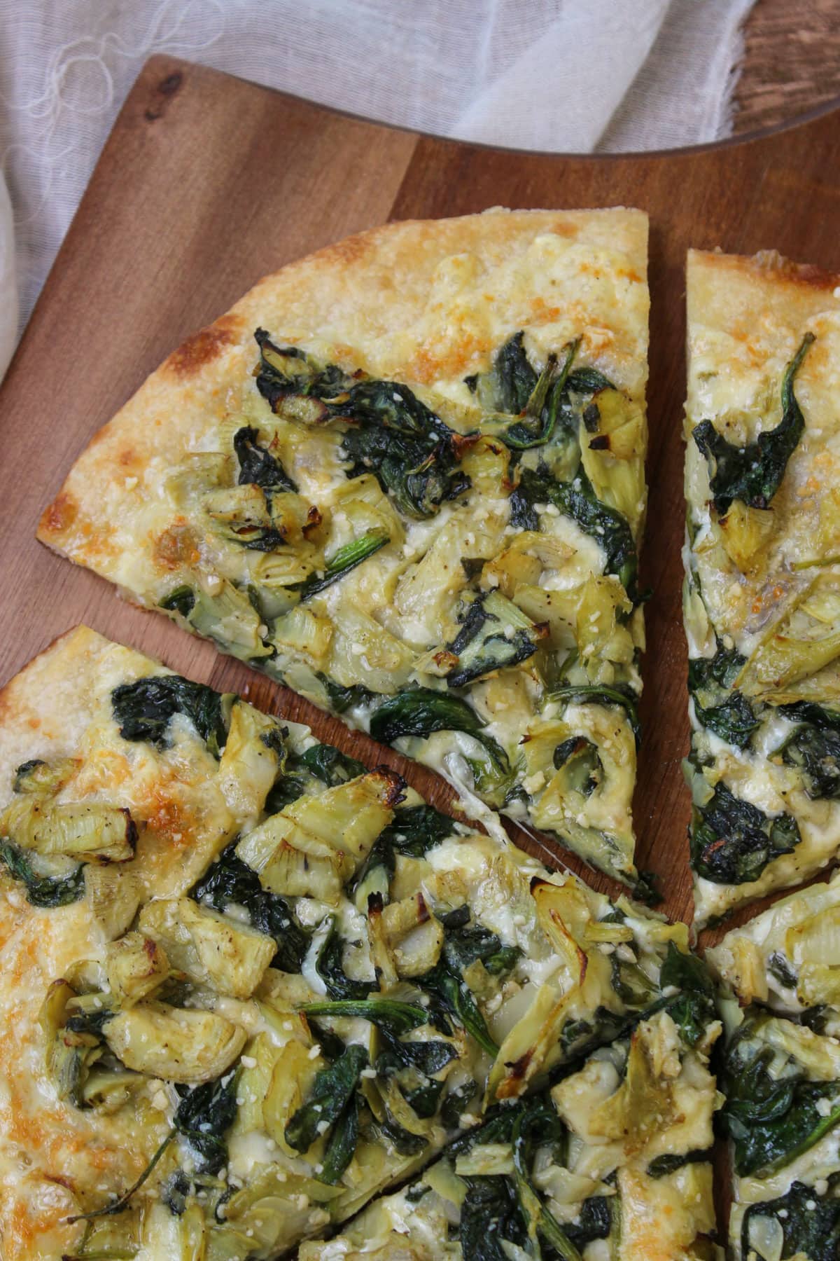 A slice of spinach and artichoke pizza on a wooden pizza peel.
