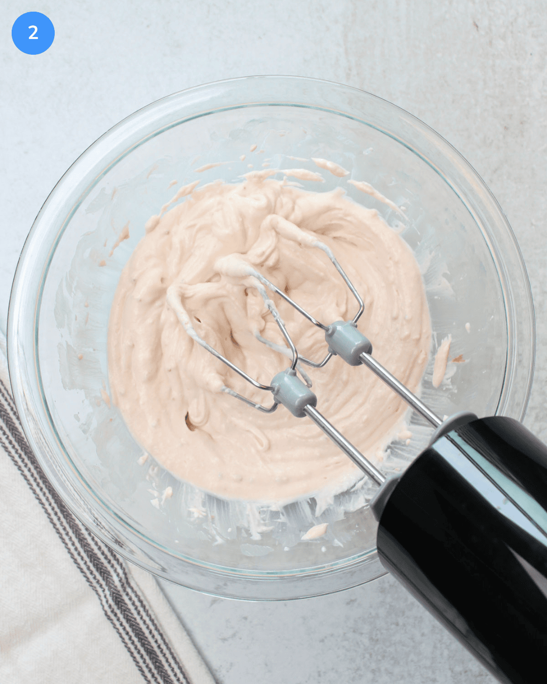 A glass mixing bowl of freshly whipped strawberry fruit dip being blended with a hand mixer.