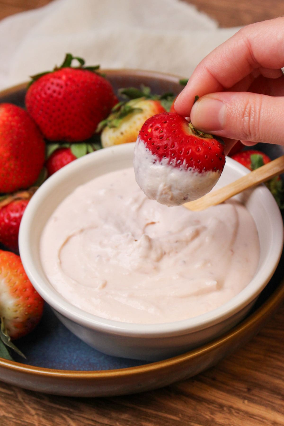 A fresh strawberry being dipped into a creamy strawberry fruit dip.