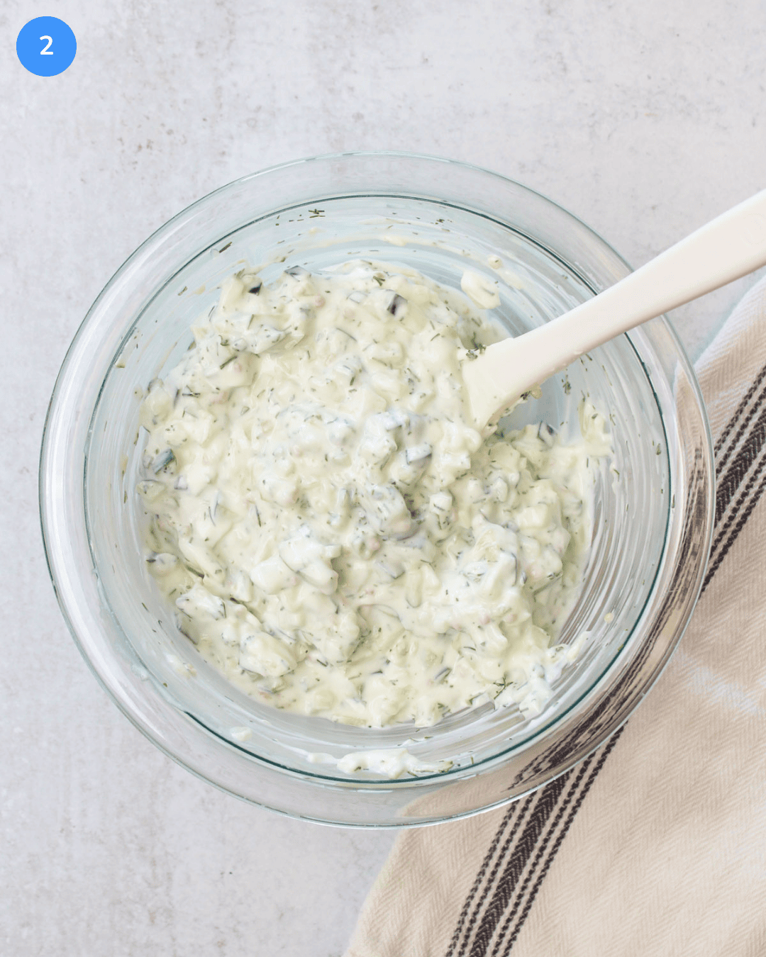 A glass mixing bowl with freshly made tzatziki in it.