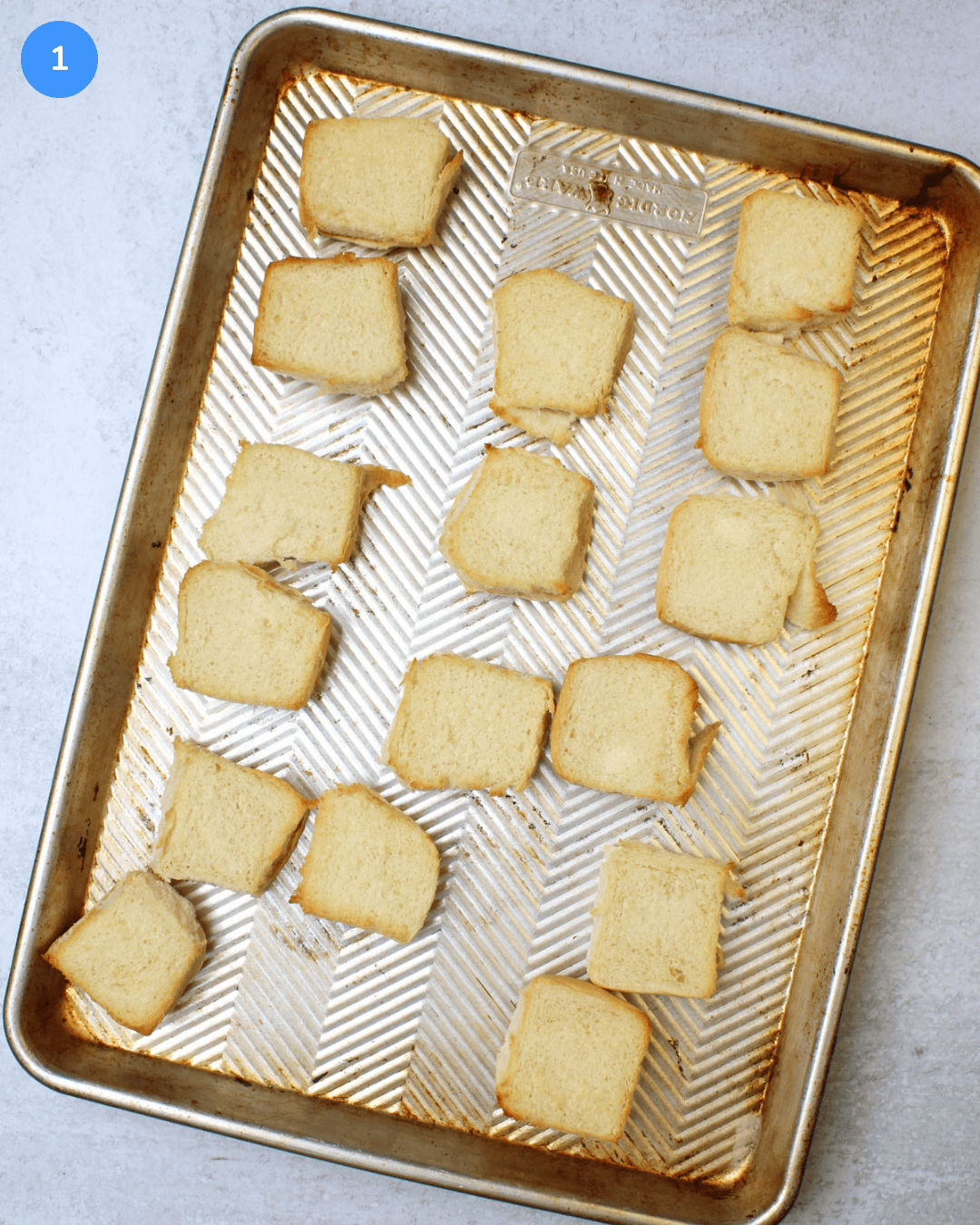 Toasted open face slider rolls on an aluminum baking sheet.
