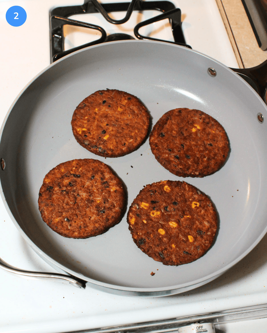 Four frozen black bean burger patties cooking on the stove in a ceramic nonstick saute pan.