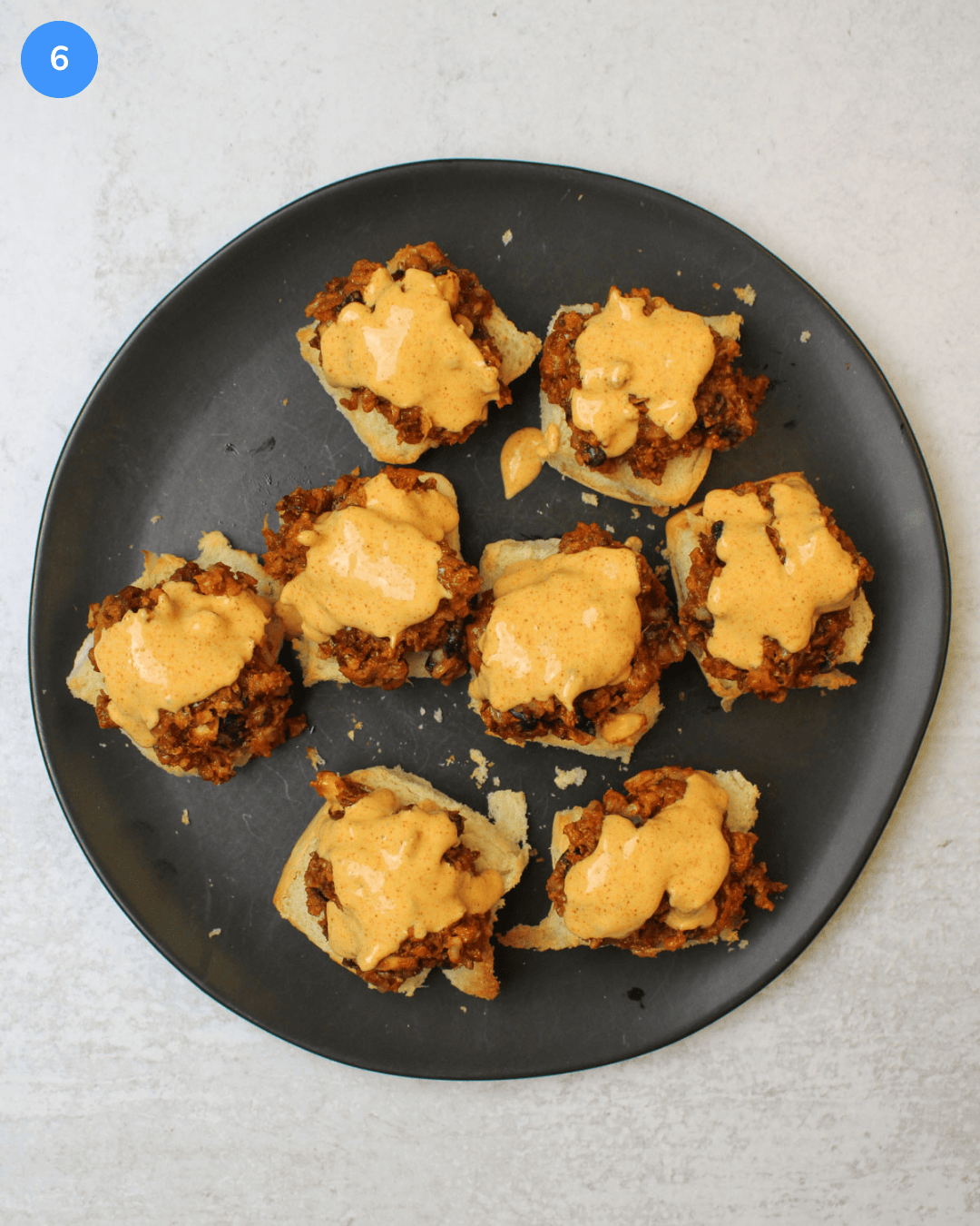 A black plate of southwest black bean sliders drizzled with chili lime dressing on hawaiian rolls.