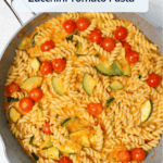 A ceramic saute pan of freshly cooked rotini with zucchini and tomatoes with a title overlaid.