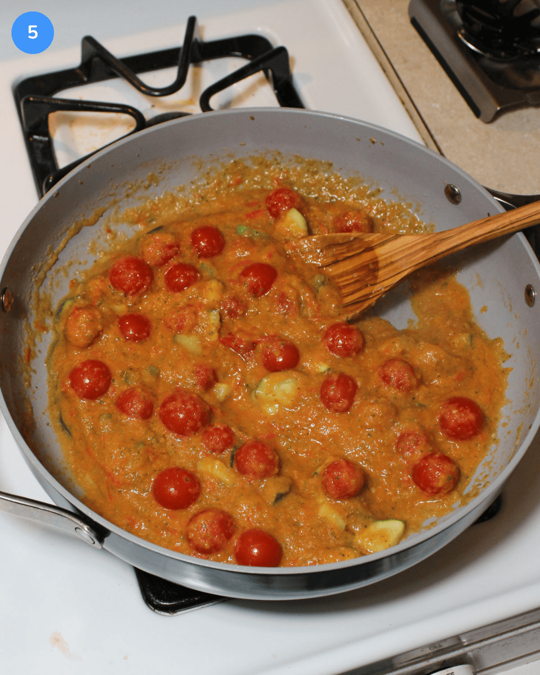 A ceramic saute pan with cherry tomatoes, zucchini, and a light tomato zucchini sauce.