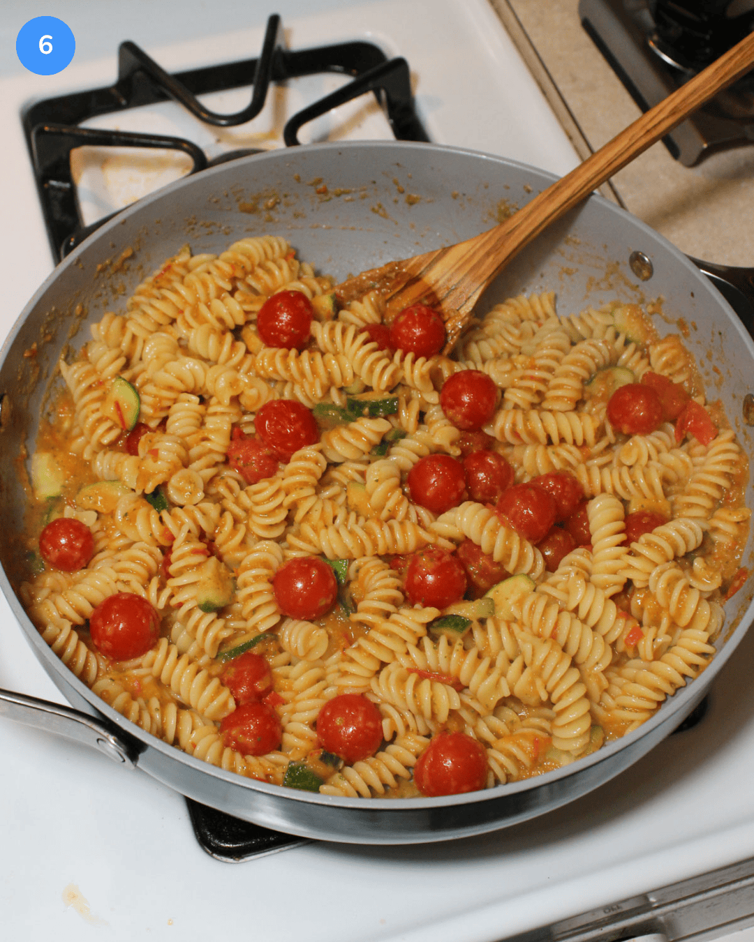 A ceramic saute pan with pasta, cherry tomatoes, and zucchini tossed in a light tomato zucchini sauce.