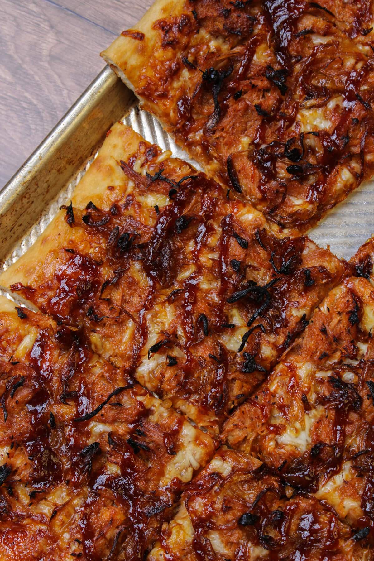 Square slices of barbecue pork pizza on an aluminum sheet pan.