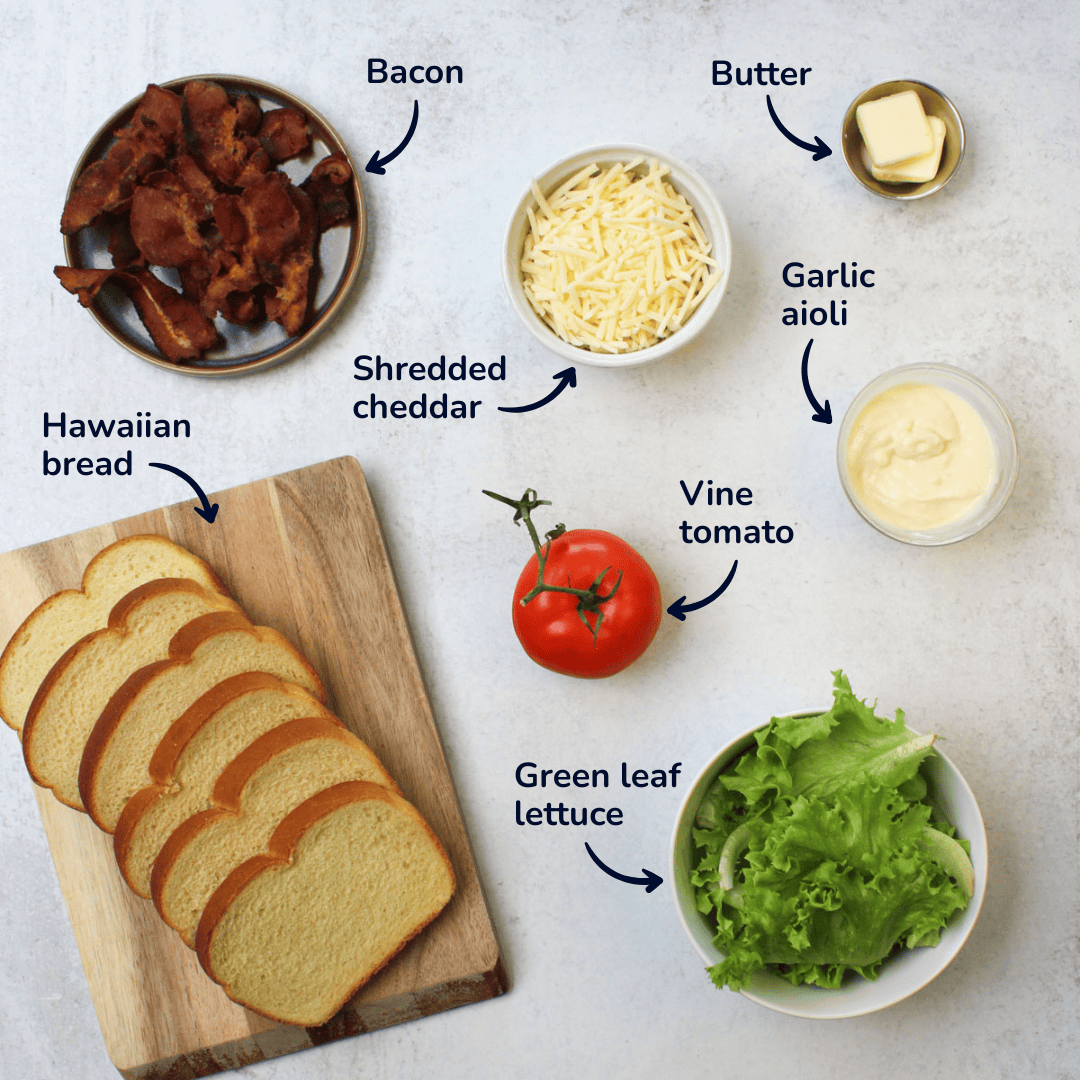 Ingredients for making a blt club sandwich: bacon, shredded cheddar, butter, garlic aioli, vine tomato, green leaf lettuce, and hawaiian bread.