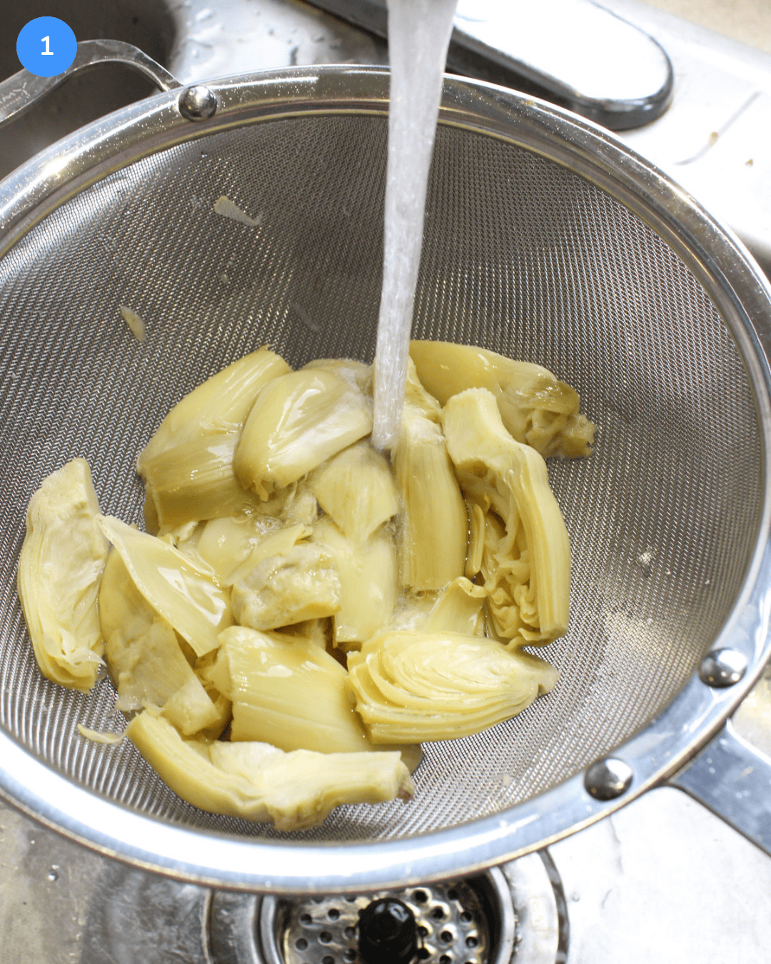 Quartered artichoke hearts from a can being rinsed under water in a mesh sieve.