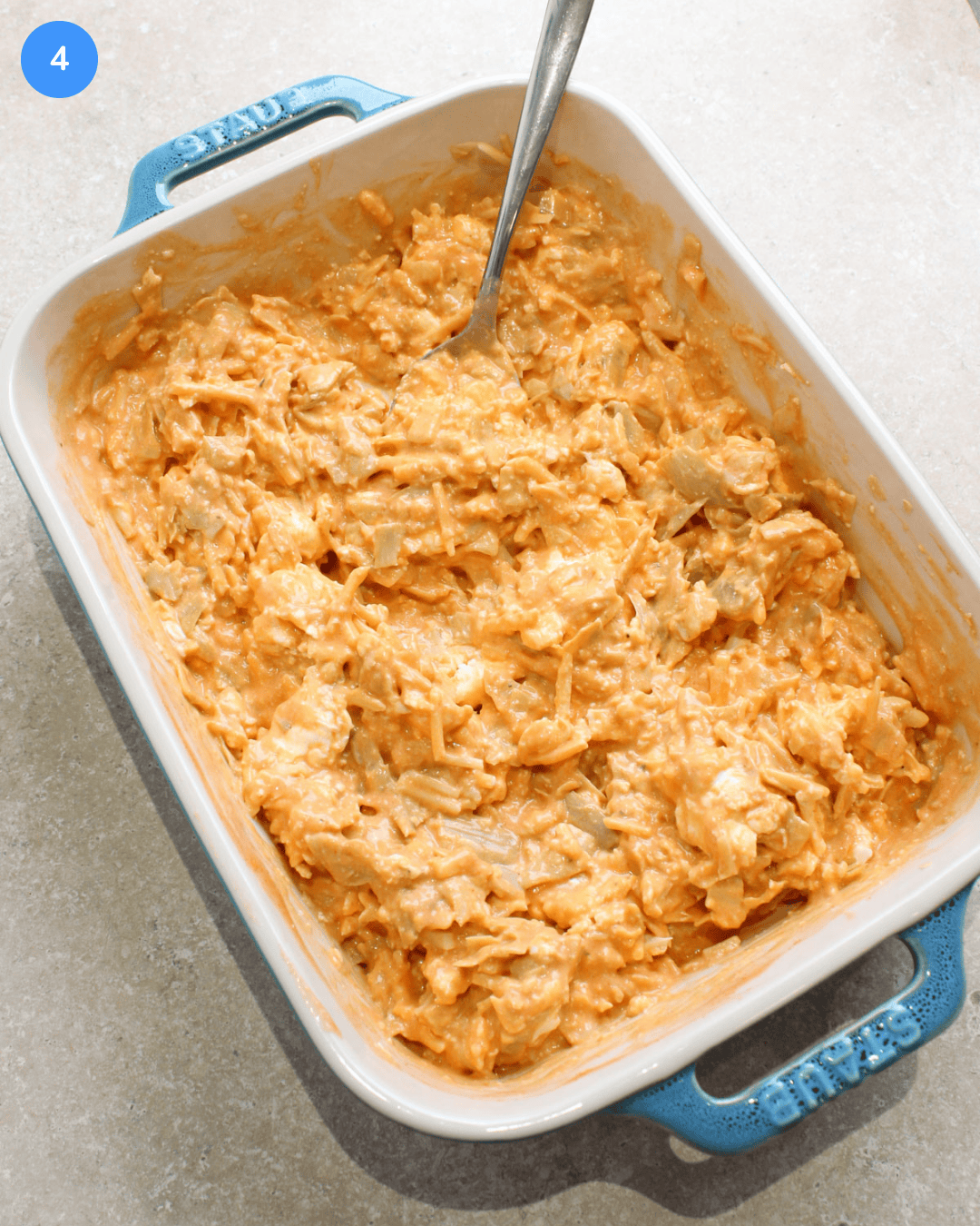 A ceramic baking dish with buffalo artichoke dip ingredients mixed together in it, before baking.