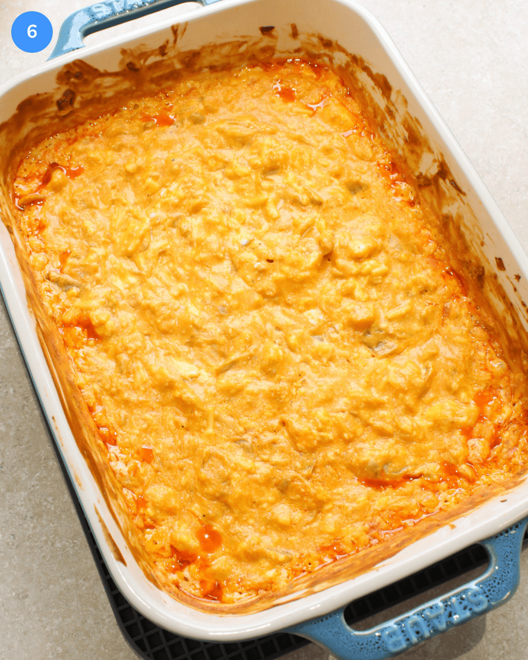 A large ceramic baking dish of hot, cheesy buffalo artichoke dip fresh out of the oven.